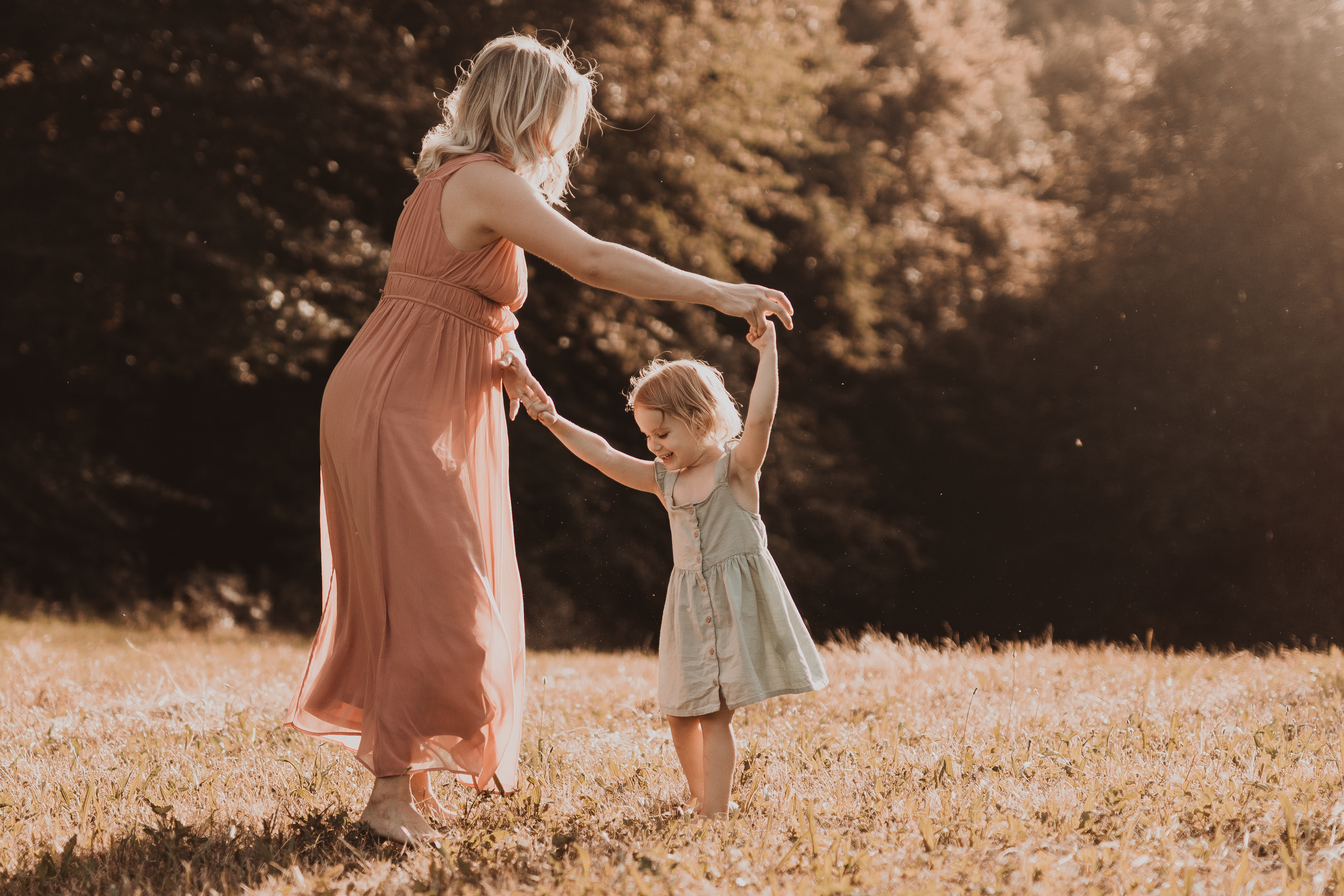 Eine junge Mutter im pastel rosa Kleid tanzt in der Abendsonne mit ihrer kleinen Tochter, die ein mintgrünes Kleidchen trägt. Die Fotografin hat den Moment der Freude zwischen Mutter und Tochter perfekt eingefangen.