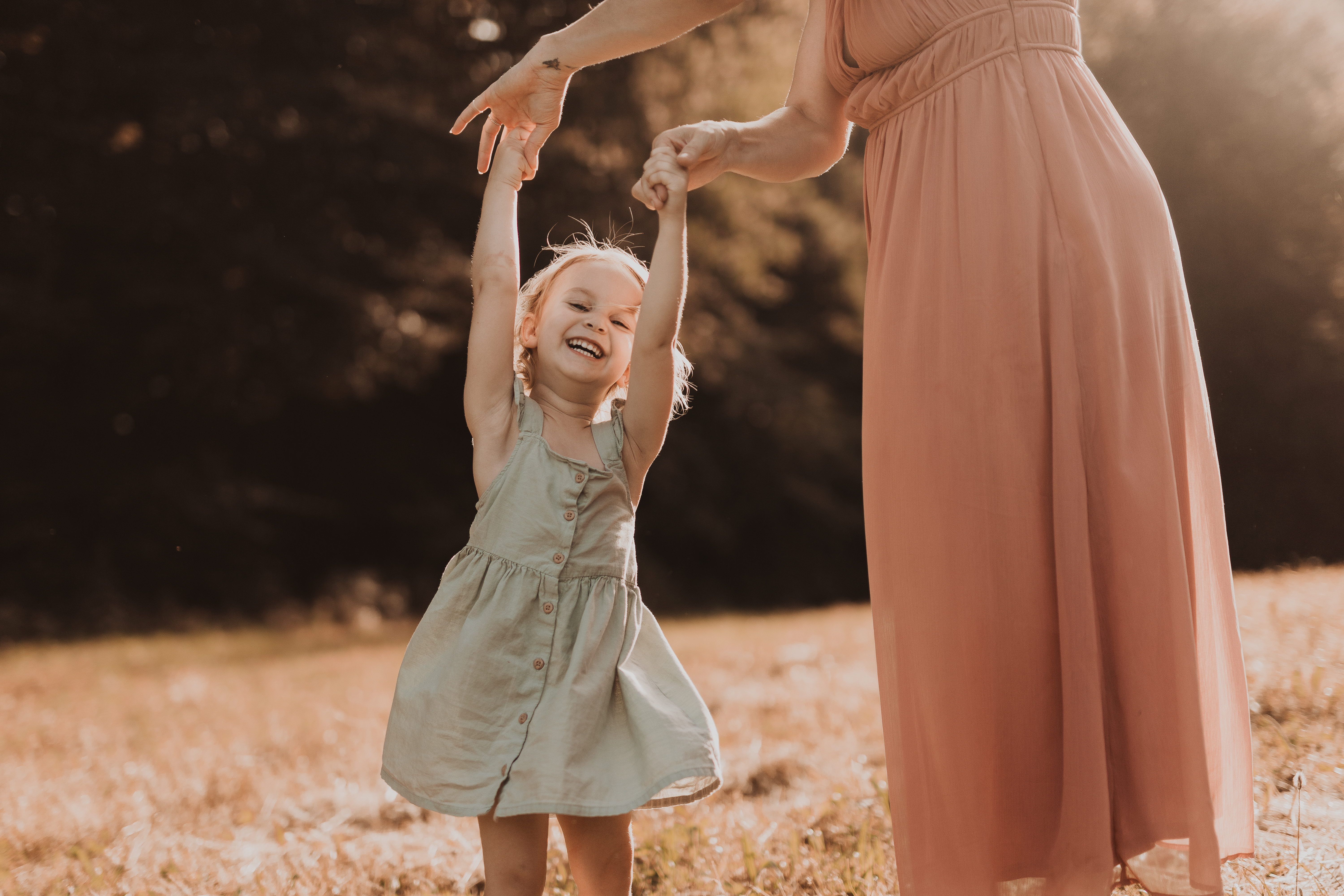 Mutter und Tochter tanzen bei einem Fotoshooting in goldener Abendstimmung zusammen. So macht ein Fotoshooting auch Kindern Spass! Aufgenommen wurde das natürliche Foto von der Fotografin Tasha Ender aus Baden.