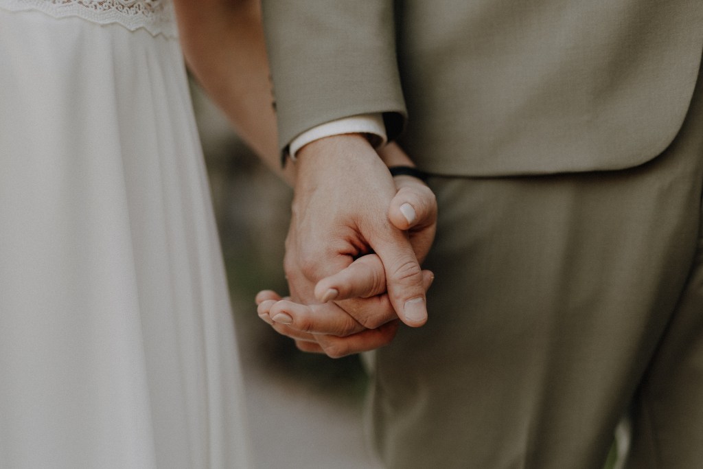 Nahaufnahme von Braut und Bräutigam, die sich an den Händen halten. Ihre verschränkten Finger sind vor der Kulisse der Villa Boveri in Baden während einer Hochzeitsfotografie-Sitzung von Tasha Ender Photography hervorgehoben. Das weiße Spitzenkleid der Braut und der hellgraue Anzug des Bräutigams rahmen diesen romantischen Moment ein, der wahrscheinlich Teil ihrer Hochzeitsfeier ist.