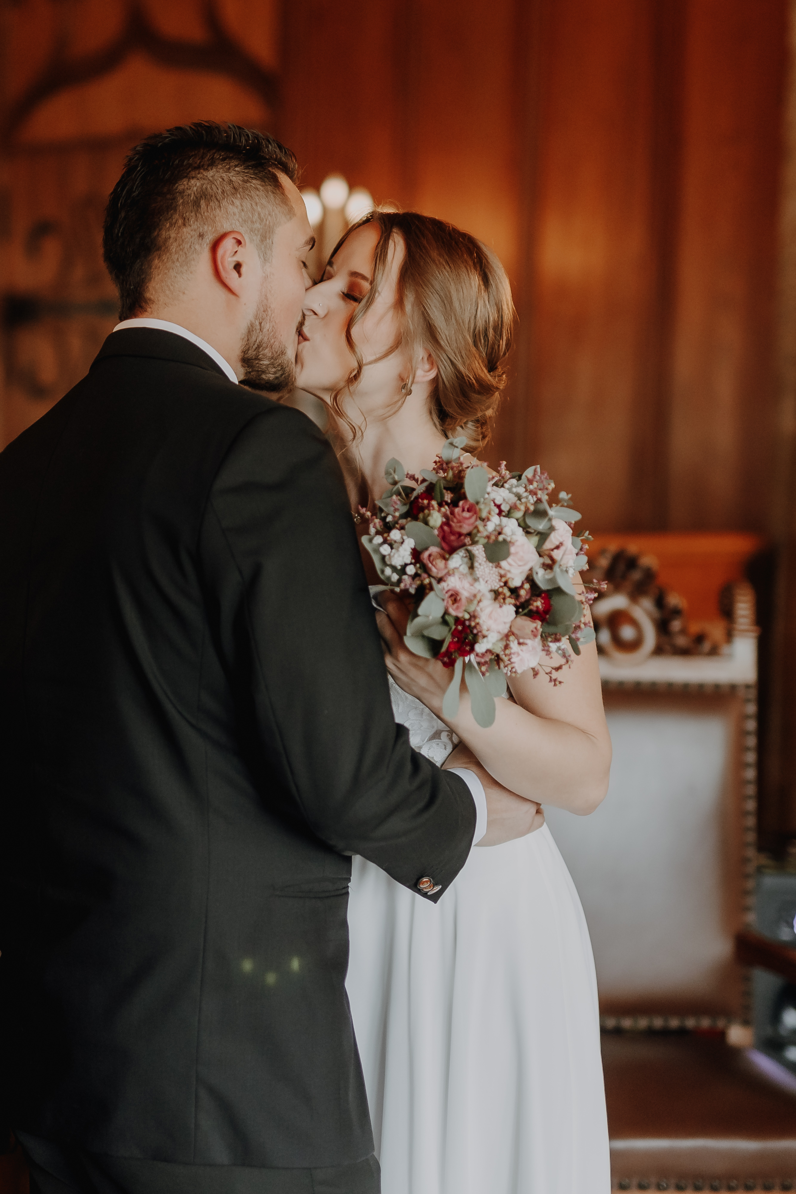 Braut und Bräutigam küssen sich drinnen während ihrer Aargauer Zivilhochzeit. Die Braut hält einen Strauß rosa und weißer Blumen mit Grünakzenten in der Hand, während der Bräutigam in Schwarz gekleidet ist. Sie stehen in einem eleganten Saal mit holzgetäfelten Wänden und dekorativen Stühlen und schaffen eine malerische Szene, die ideal für ihr Fotoshooting von Tasha Ender Photography's Hochzeitsfotografie ist.
