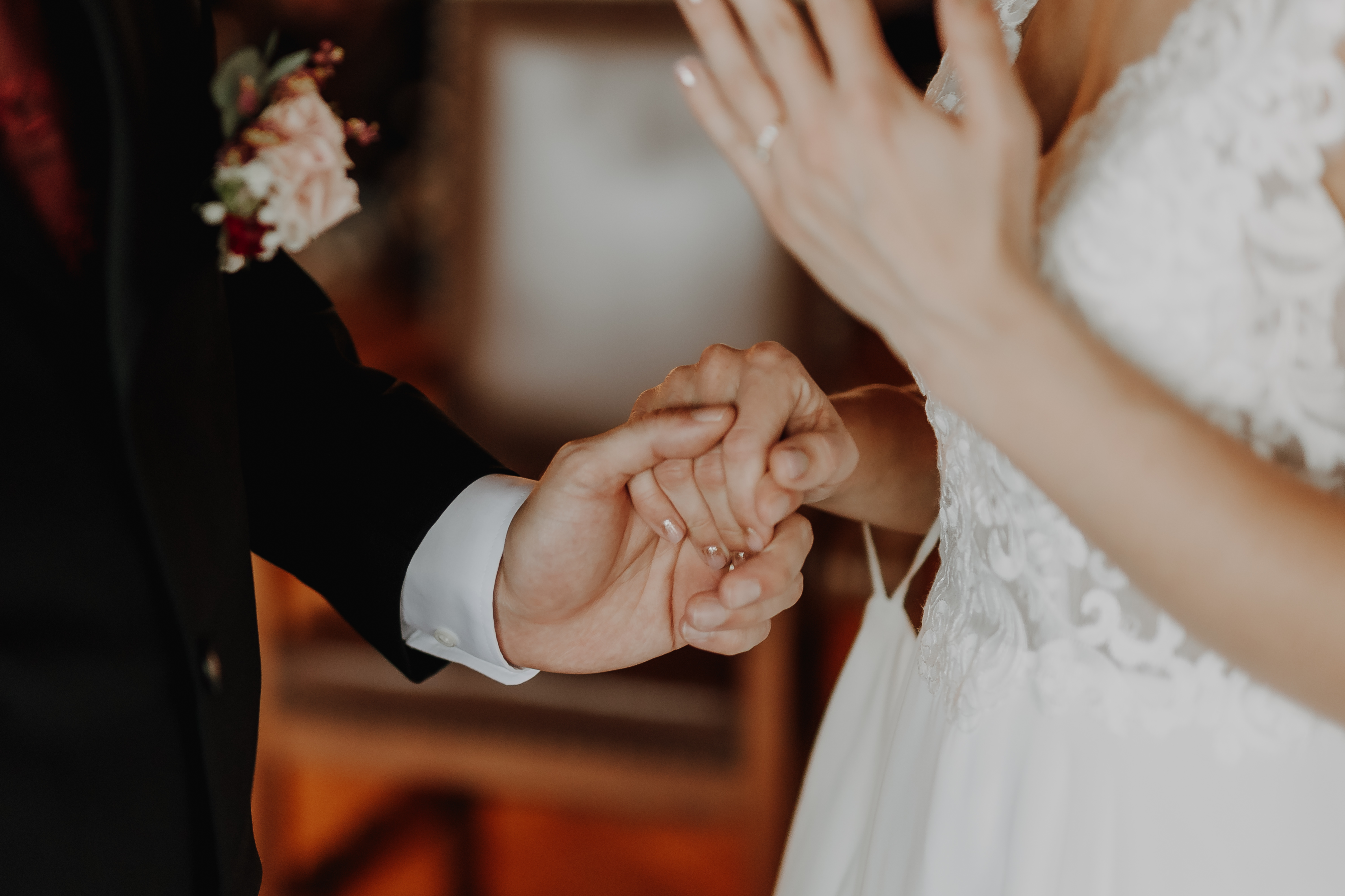 Nahaufnahme eines Paares, das während seiner Zivilhochzeit Händchen hält. Die Person rechts trägt ein weißes Spitzenbrautkleid und zeigt einen Ring. Der Hintergrund ist unscharf, was den intimen Moment betont, der in dieser wunderschönen Hochzeitsfotografie von Tasha Ender Photography festgehalten wurde.