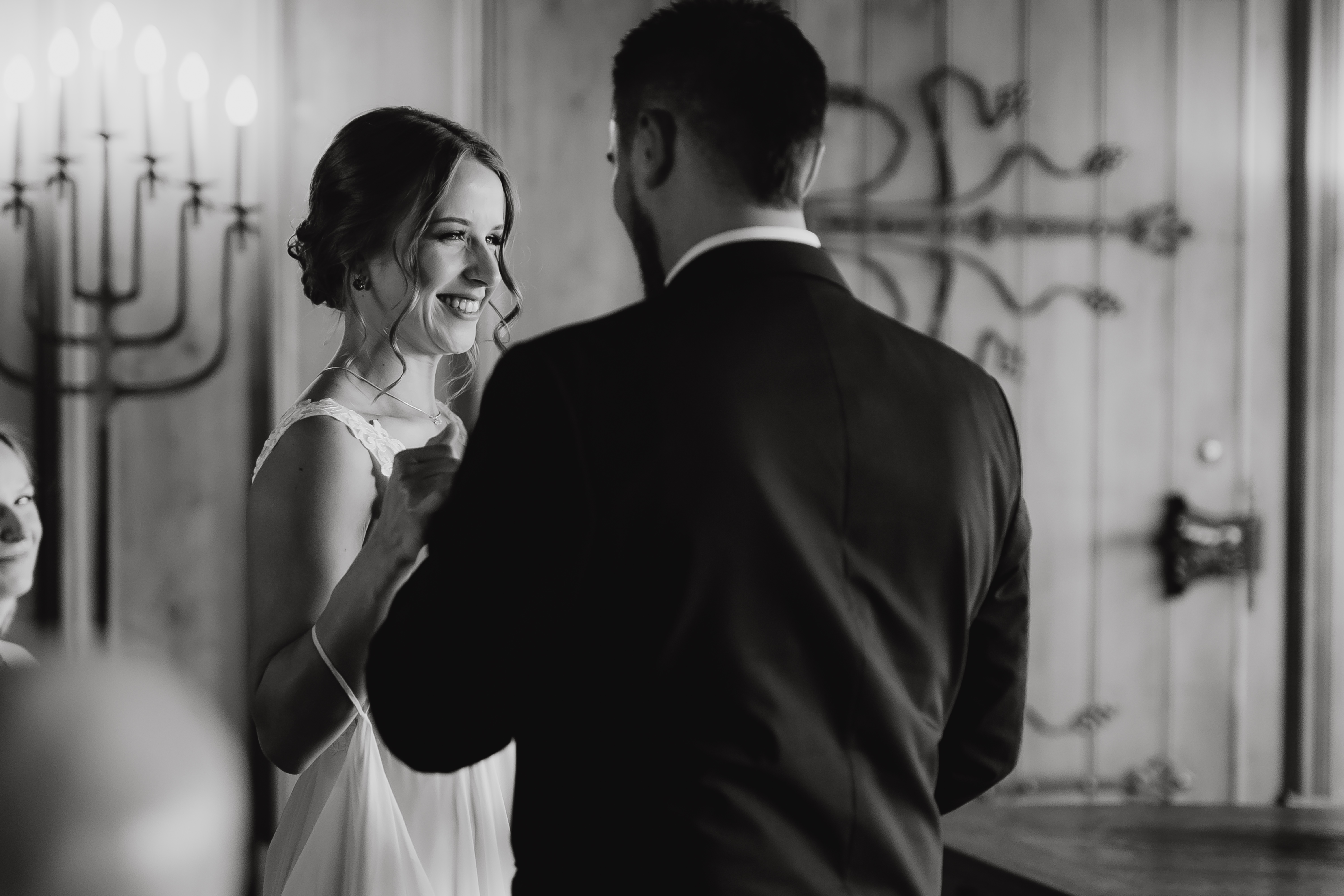 Ein Schwarzweißfoto von Tasha Ender Photography zeigt Braut und Bräutigam, die bei ihrer Ziviltrauung tanzen und lächeln. Die Braut trägt ein ärmelloses Hochzeitskleid und der Bräutigam einen dunklen Anzug. Sie sind in einem elegant dekorierten Holzraum mit einem Kerzenständer im Hintergrund zu sehen – ideal für zeitlose Hochzeitsfotografie.