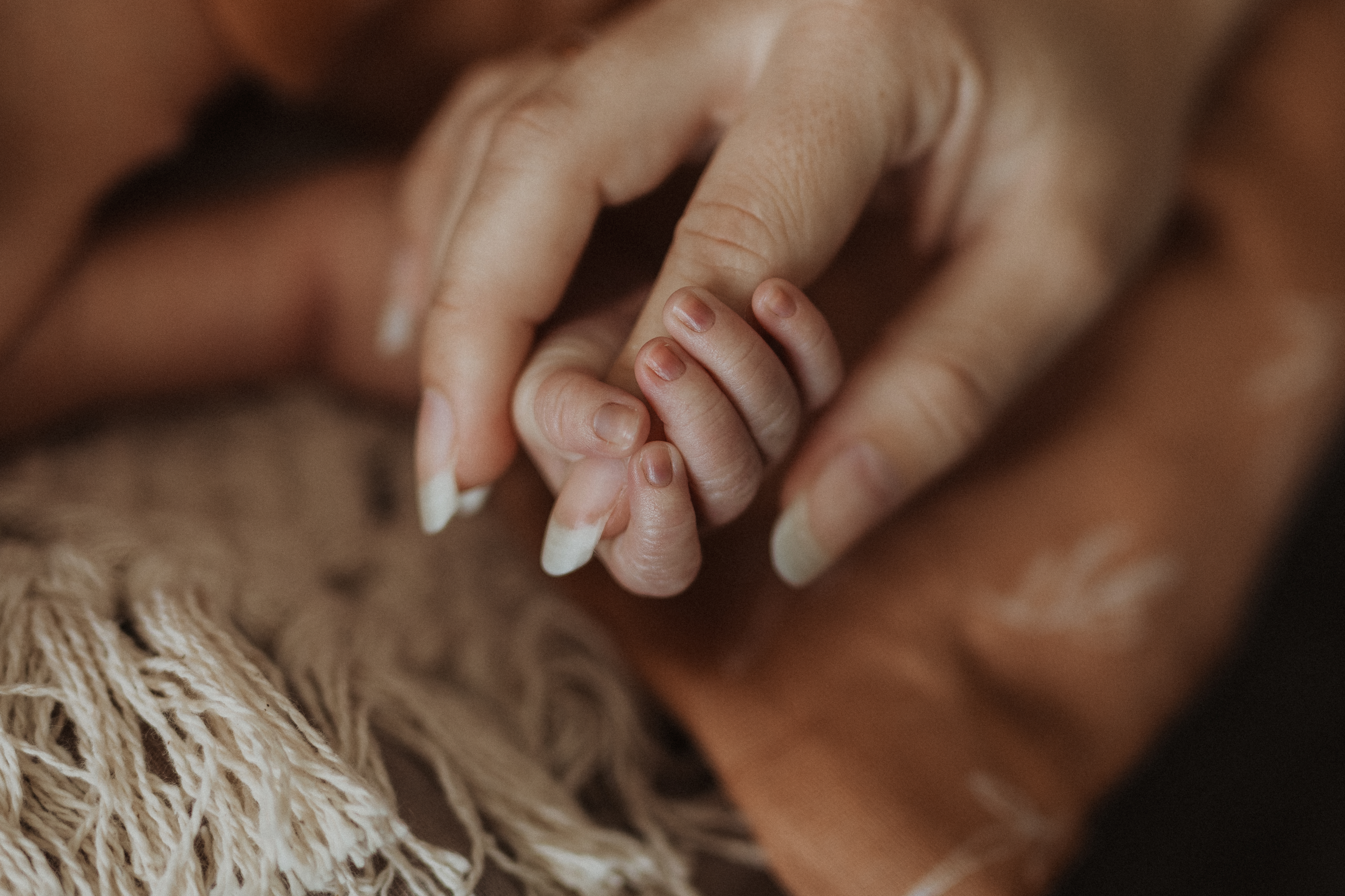Die kleinen Finger eines neugeborenen Kindes schliessen sich um den Zeigefinger der Mutter. Ein emotionaler Moemnt zwischen Mutter und Kind, eingefangen von der Newborn-Fotografin aus Baden.