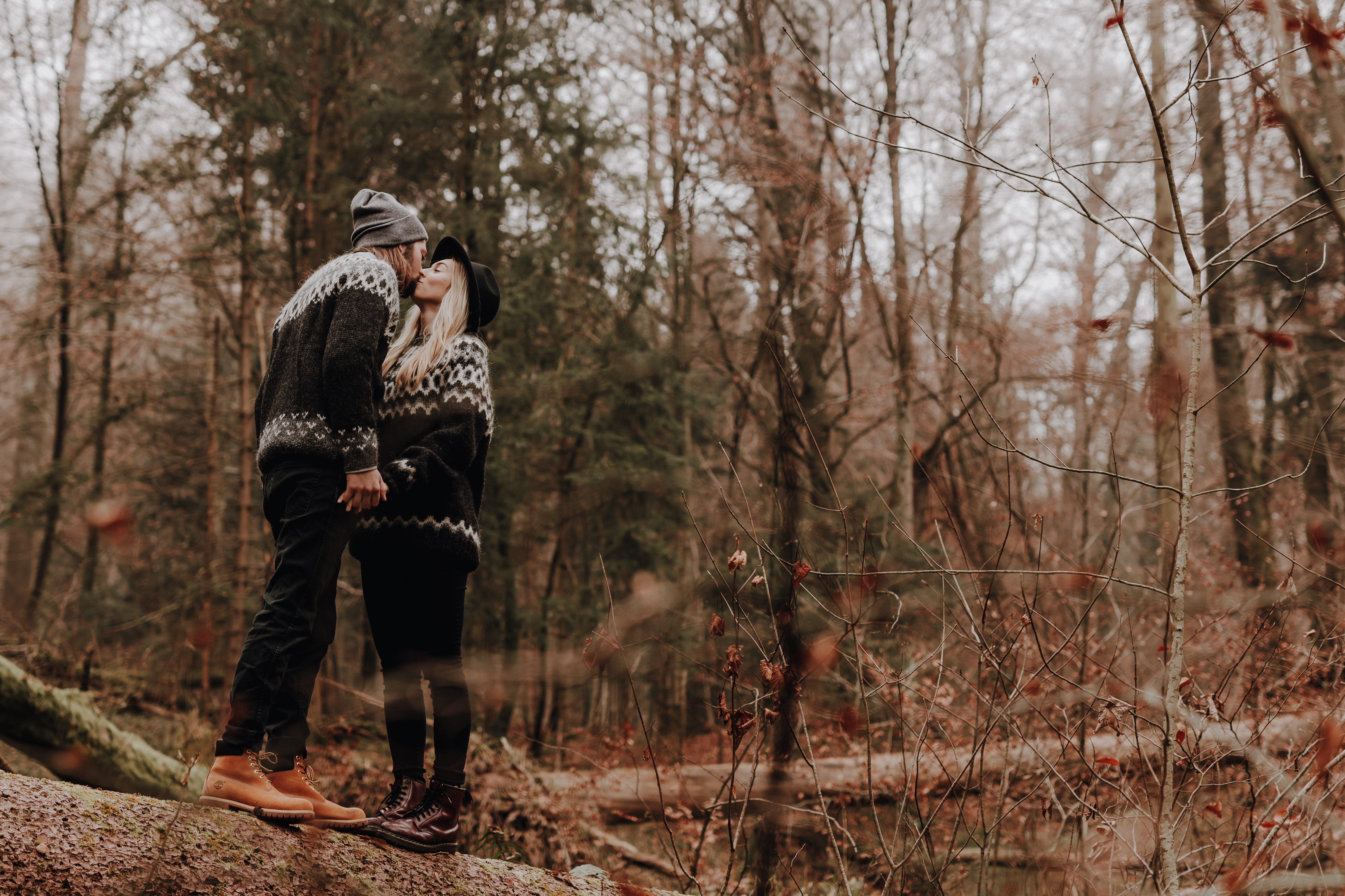 Ein Paar steht mitten im Wald, Die beiden Küssen sich. Beide tragen dicke Winter-Pullover während dieses Fotoshootings im Wald mit der Fotografin Tasha Ender.