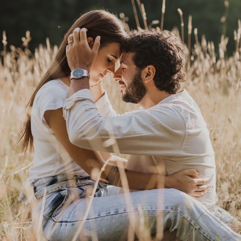 Ein Paar sitzt im hohen Gras und schaut sich zärtlich in die Augen. Eine emotionale, ungestellte Momentaufnahme während eines Paarshootings mit der Fotografin.