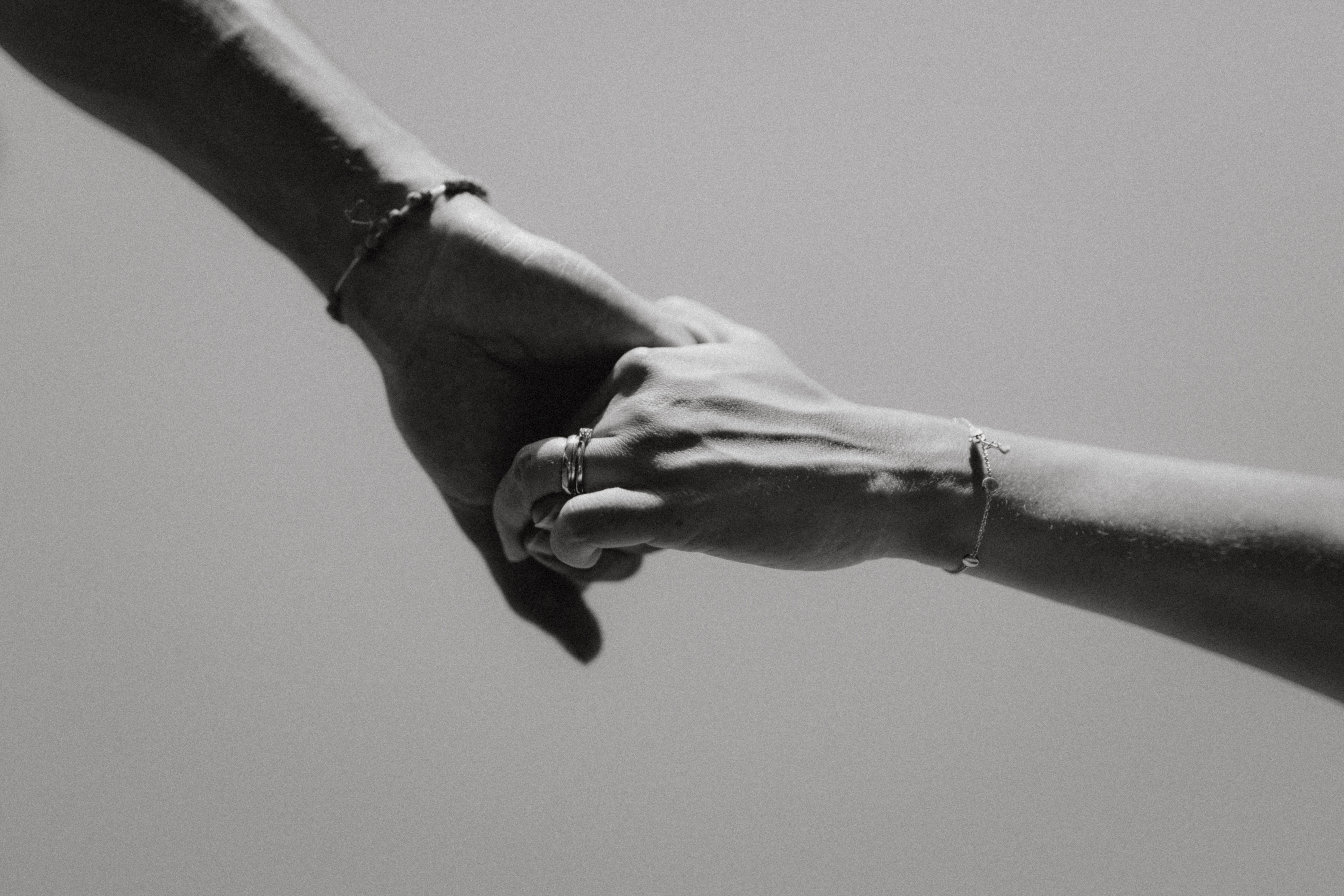 Zwei Hände, die sich in einem Schwarz-Weiß-Bild halten, aufgenommen von Fotografin Tasha Ender. Beide Hände tragen Armbänder, eine Hand ist mit einem Ring geschmückt. Der Hintergrund ist schlicht und unscharf und lenkt die ganze Aufmerksamkeit auf die innige Verbindung zwischen den Händen bei diesem Fotoshooting.