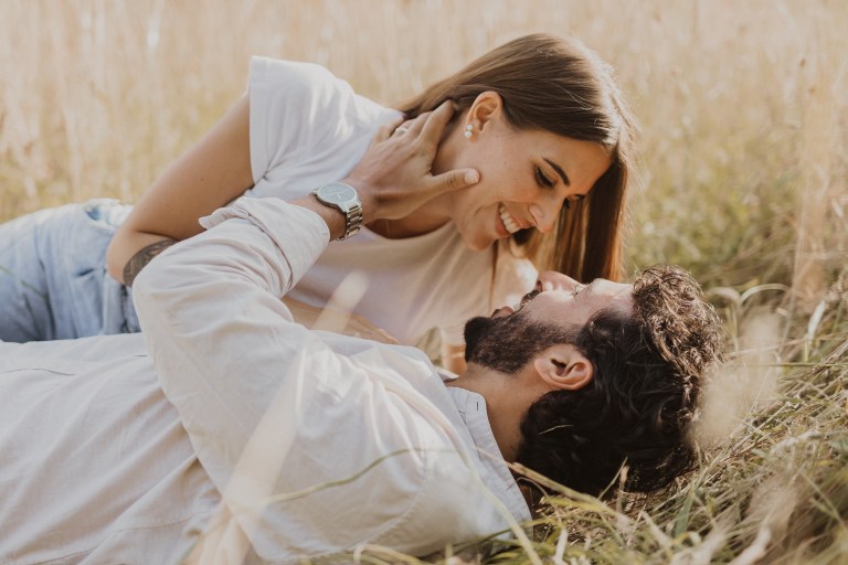 Ein Paar liegt in einer Wiese und schaut sich verliebt in die Augen. Ungestellte, natürliche Paaraufnahme während eines Fotoshootings in Baden.