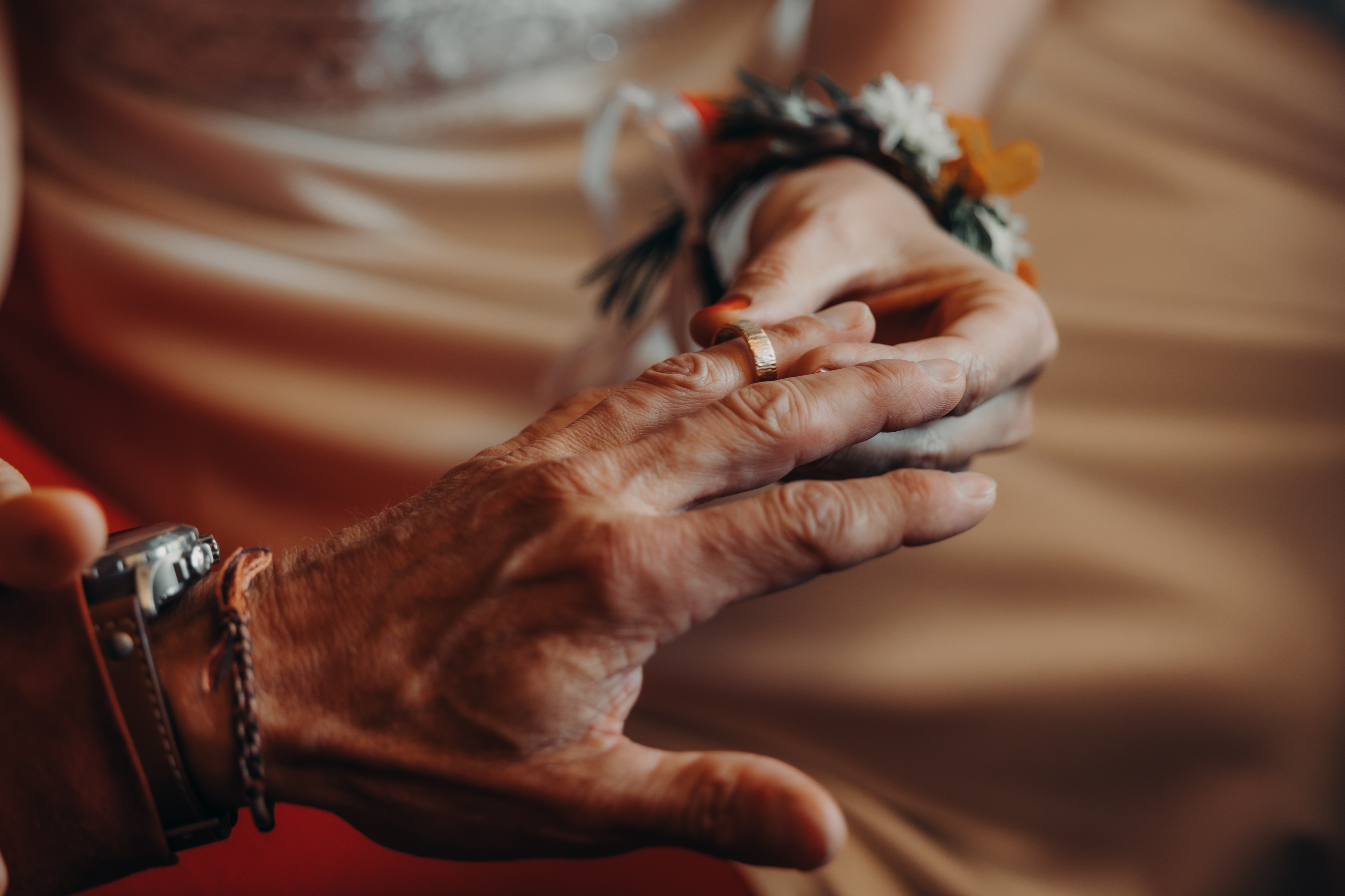 Nahaufnahme einer Person, die einer anderen während einer Ziviltrauung einen Ehering an den Finger steckt, aufgenommen von Tasha Ender Photography's Hochzeitsfotografie. Beide Personen sind in formeller Kleidung gekleidet; die Person, die den Ring erhält, trägt ein Blumenanstecker am Handgelenk, während die andere mit einer Uhr und einem Armband geschmückt ist.