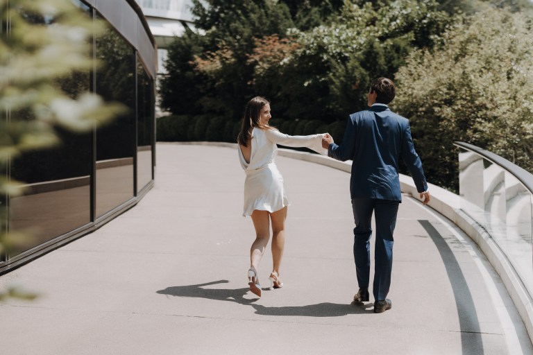 Ein frisch verheiratetes Paar schreitet freudig, Hand in Hand, entlang einer Strasse beim Dolder Grand Hotel in Zürich. Perfekt eingefangene Momentaufnahme der erfahrenen Hochzeitsfotografin Tasha Ender aus Baden.